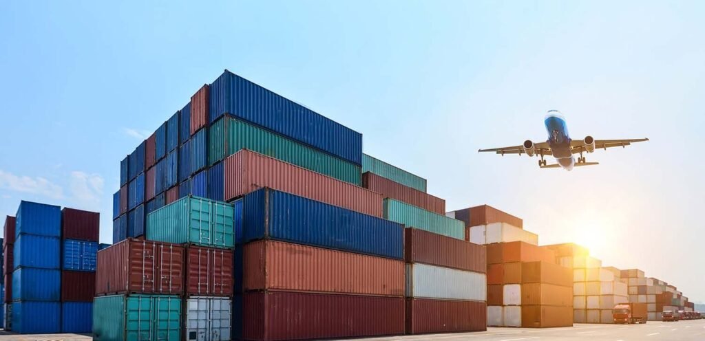 Stacked shipping containers in an industrial port container yard beside an office building, with a cargo plane overhead, illustrating export freight for bulk orders