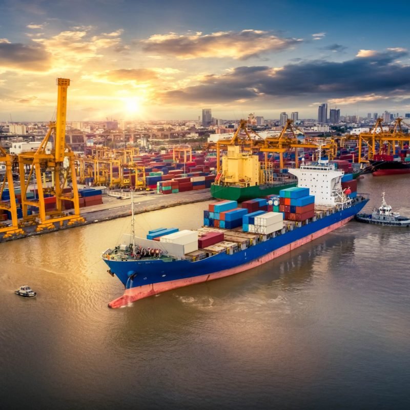 Container ship at a busy port with gantry cranes and stacked shipping containers at sunset